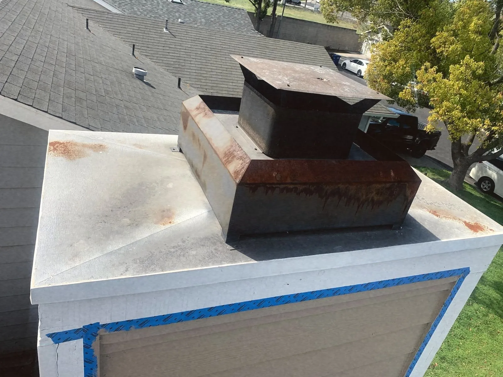 A black chimney cap on a white chase top, taped off for paint