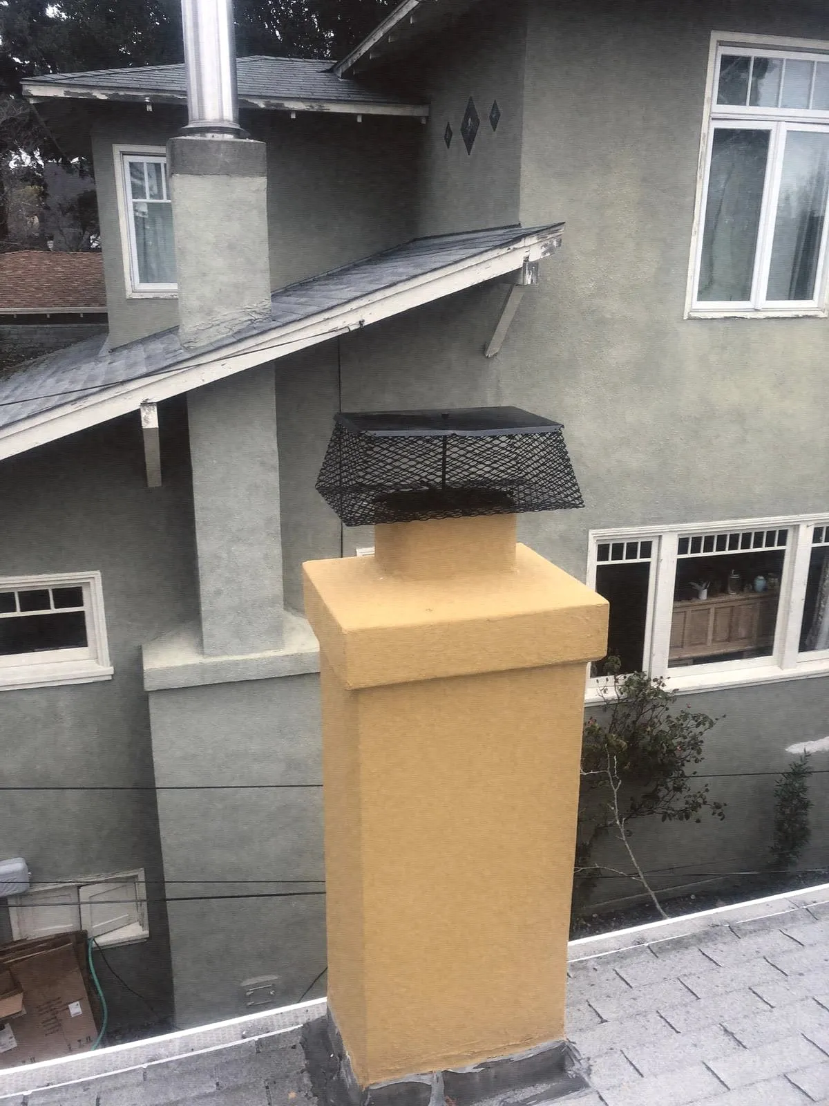 A black mesh cap on a stucco chimney chase top